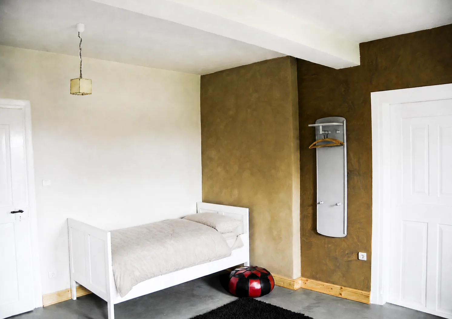 Einzelbett vor heller Wand mit Garderobe im selben Zimmer